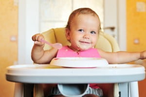 Lachende baby in kinderstoel met bordje pap